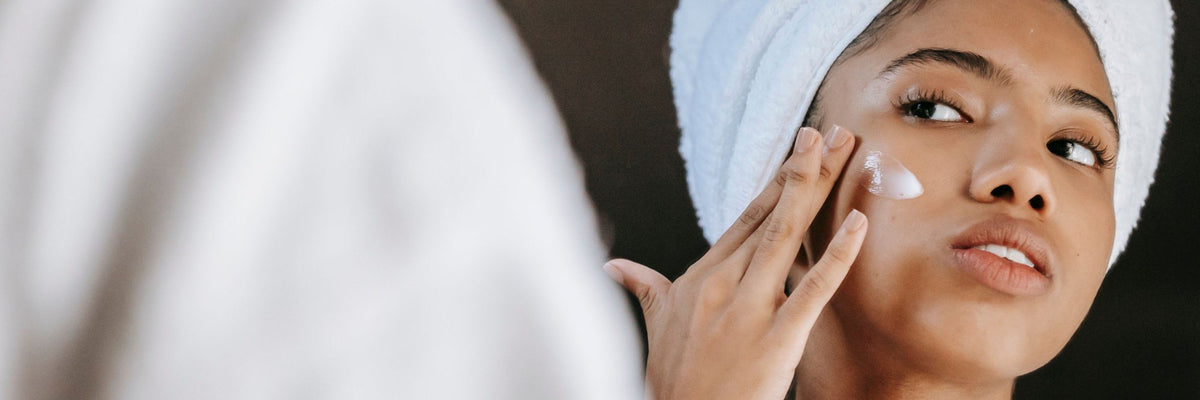 Woman with a towel wrapped around her hair, smoothing moisturiser onto her cheek
